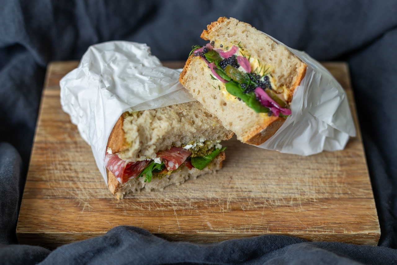 Bunt belegte Sandwiches gewickelt in Butterbrotpapier auf Holzbrett Flamboyant Food Fotografie